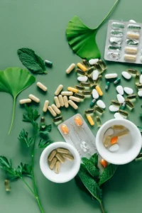 Assortment of probiotic and herbal supplement capsules on a green background with fresh mint and ginkgo leaves — natural gut health support.